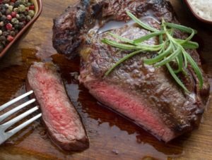 medium roast rib-eye steak on wooden plate with pepper and salt