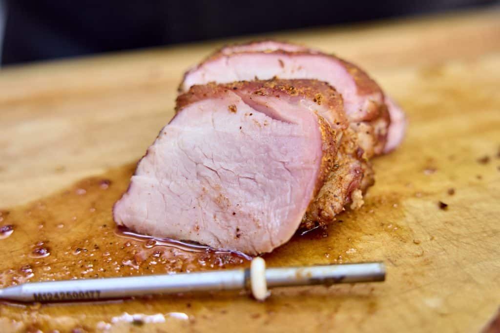 perfectly cooked, juicy pork tenderloin with thermometer probe in foreground