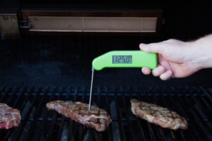 Checking a steak on the grill with a Classic Thermapen