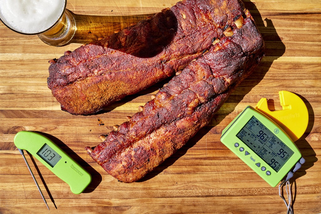 Dry rubbed ribs on a cutting board with thermometers