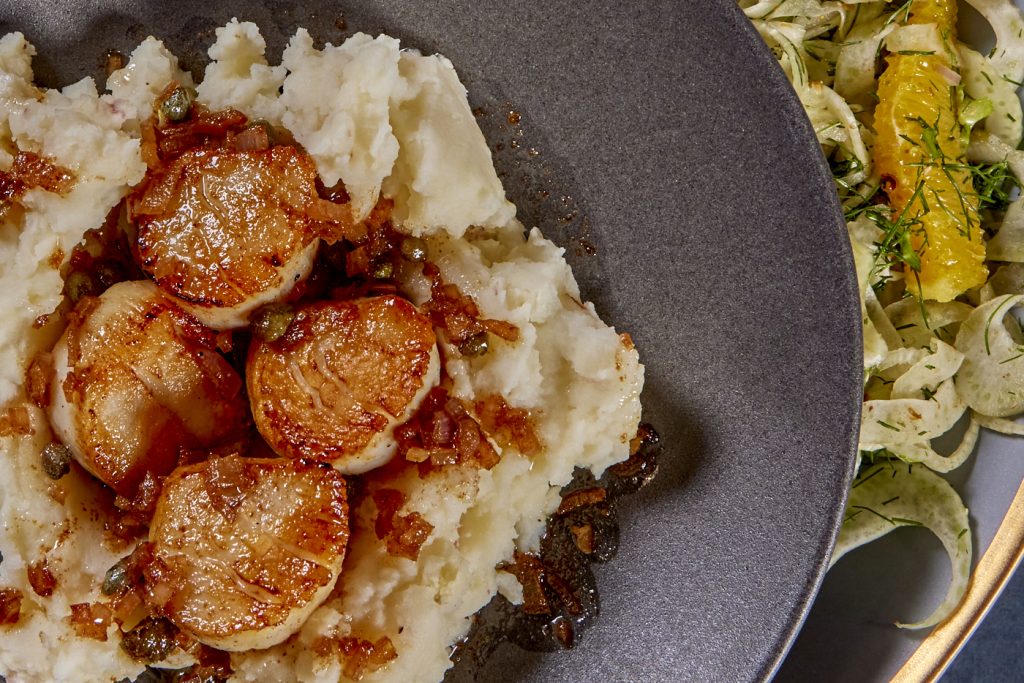 Seared scallops with sauce on a bed of potatoes
