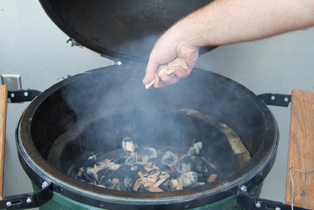 Sprinkling wood chips onto the coals of an egg-type smoker.