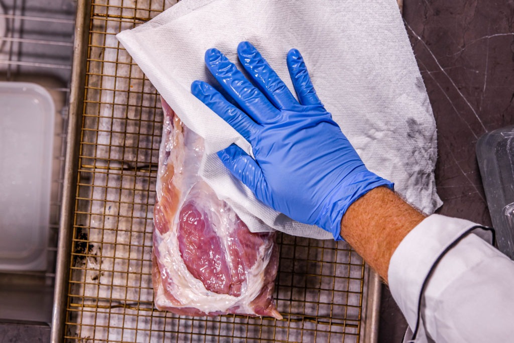 Patting the cured loin dry with paper towels.