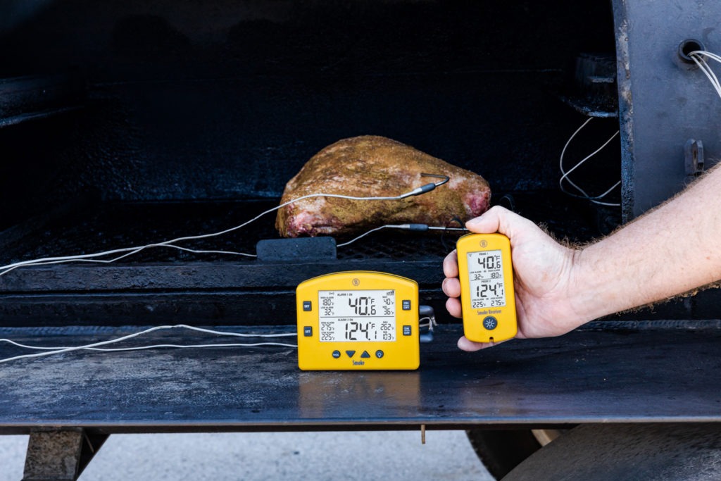 A seasoned lamb shoulder in a smoker with probes and a thermometer