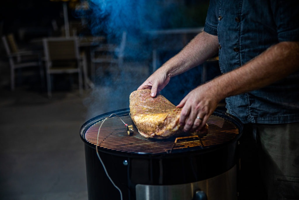 Placing a seasoned brisket on a  preheated smoker