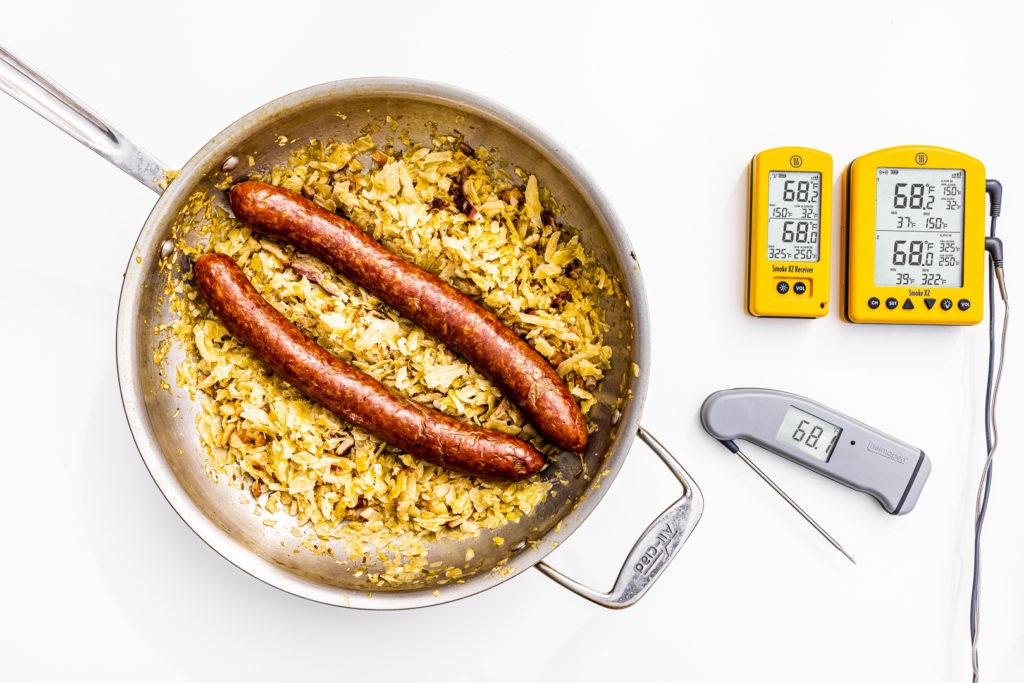 Kielbasa in a pan of sauerkraut next to some thermometers