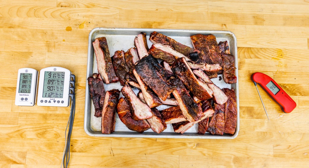 A big pile of BBQ ribs with the thermometers used to cook them