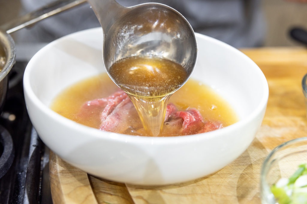 Ladling hot pho broth over raw beef