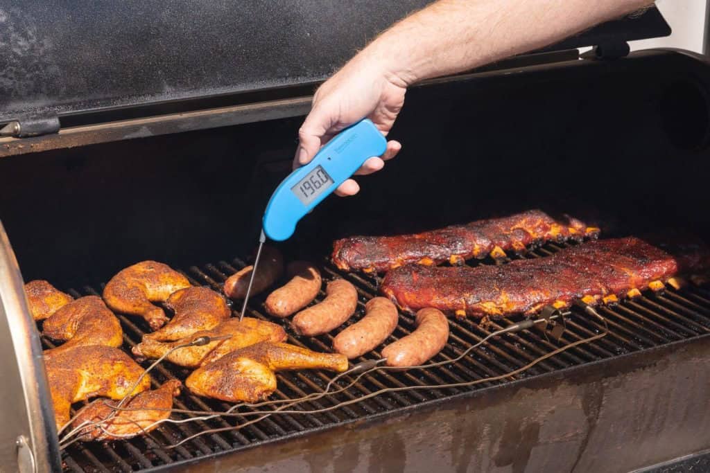 temping chicken on a smoker grate full of meats