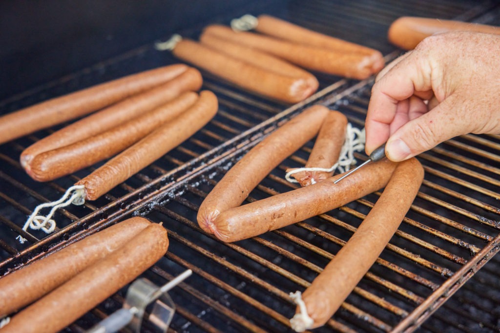 inserting a needle probe in a hotdog on the smoker. 