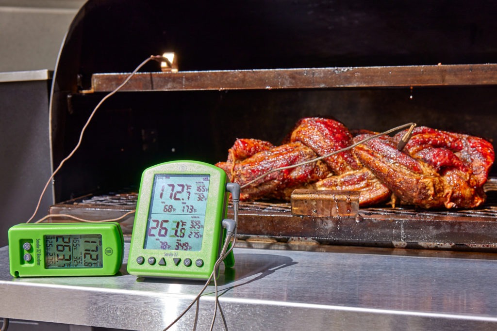 Sticky braided pork belly on the smoker with thermometer in foreground