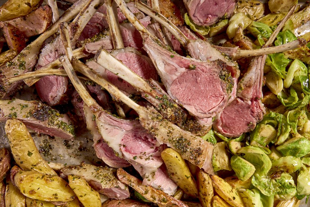 Lamb chops cut from a few racks of lamb on a bed of potatoes and pan-roasted Brussels sprouts